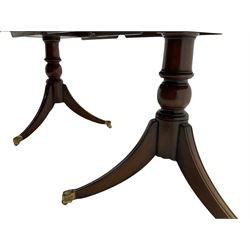 Regency style cross banded mahogany twin pedestal dining table, extending with additional leaf, on twin pillars each with three splayed supports terminating at brass paw cups and castors 