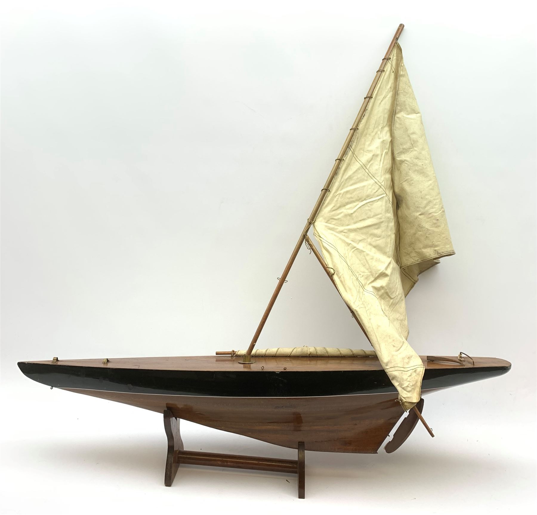 Pond yacht with part black painted mahogany hull and keel, working rudder and mast with three sails W90cm H95cm, loose mounted on mahogany stand