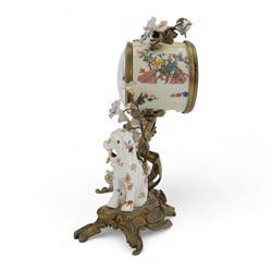 French- early 20th century 8-day Chinoiserie brass and porcelain mantel clock in the 18th century style, brass base with splayed feet profusely decorated with clusters of painted porcelain flowers and two decoratively painted Chinese foo dogs, movement enclosed in a circular porcelain movement case illustrated with birds of paradise and oriental motifs, with a white enamel dial Arabic numerals, minute markers, pierced gilt hands and a floral swag, rack striking Parisian movement striking the hours and half-hours on a bell. With a visible sunburst pendulum and key.