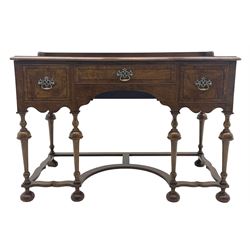20th century Queen Anne style kneehole writing table, the figured and moulded rectangular top with raised gallery back, shaped front apron fitted with three drawers, on turned supports joined by a series of shaped and curved stretchers, on turned bun feet, the central drawer set with circular ivorine label inscribed ‘Pallmall, Hamptons, London’