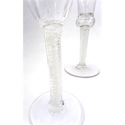 Five 18th century and later drinking glasses, comprising large example with bell shaped bowl upon single series air twist stem and spreading circular foot, H20.5cm, example with bell shaped bowl engraved with roses upon a double series opaque twist stem and spreading circular foot, H15.5cm, and a further three, two with bell shaped bowls, and one with funnel bowl, each upon double series opaque twist stem and spreading circular foot 