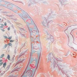 Large late 20th century Aubusson style wool carpet, peach and pastel toned field with central floral medallion enclosing scrolling acanthus and and foliate sprays, surrounding field decorated with further stylized foliage and and floral ornament, within shaped reserves and indigo corner spandrels, enclosed by narrow guard border, cotton fringe ends