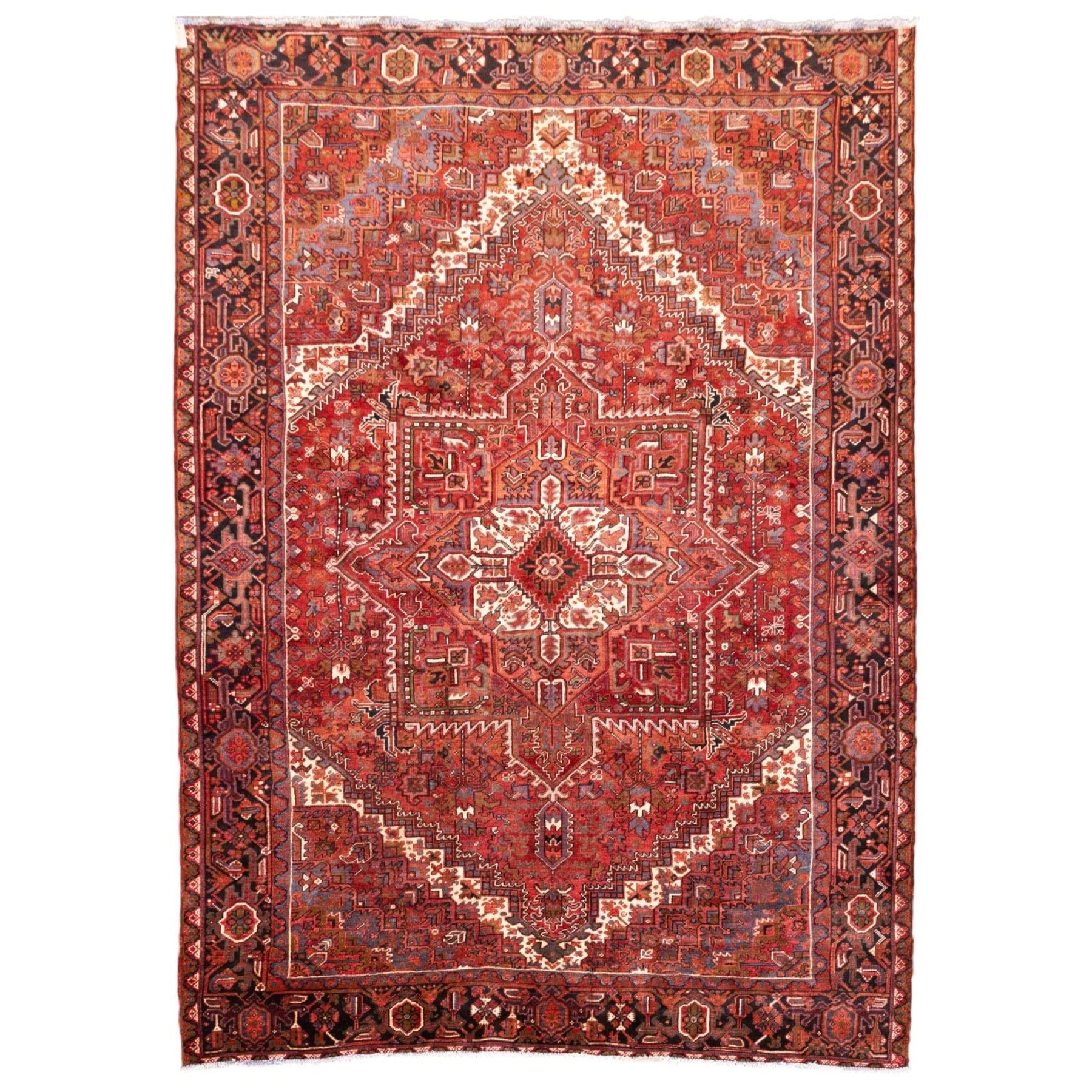 North West Persian Heriz hand-knotted carpet, madder red field, with a large central angular star medallion with stepped outlines on ivory ground, surrounded by geometric floral devices and stylized rosettes, with corresponding corner spandrels, enclosed by a bold geometric main border with multiple guard stripes, with cotton fringe ends 