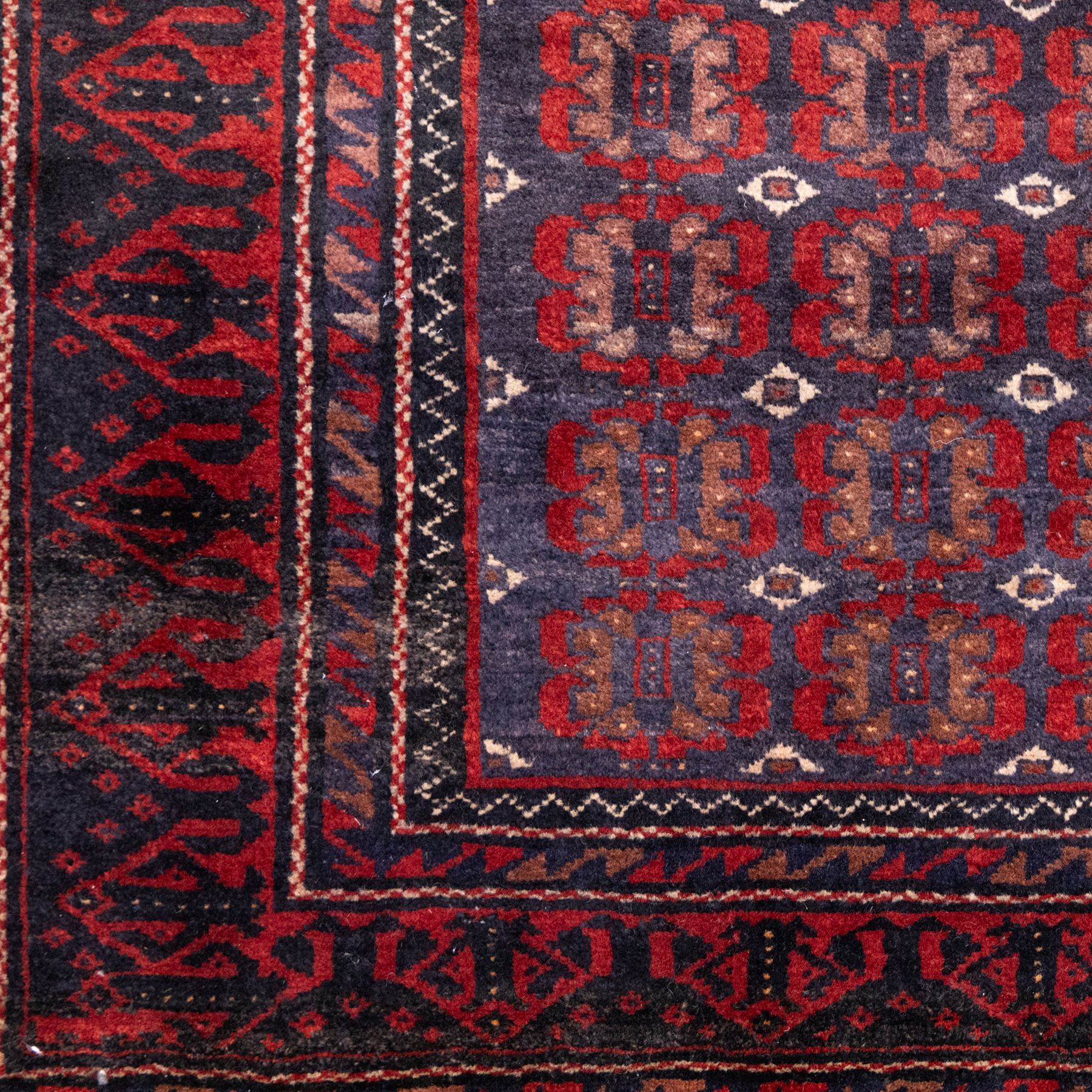 North East Persian Turkoman hand-knotted rug, indigo field densely decorated with an all-over repeating design of geometric gul motifs in shades of madder red, aubergine, and dark brown, highlighted with small ivory details, framed by multiple narrow guard borders and a main border with angular geometric motifs flanked by zig-zag borders, with cotton fringe ends 