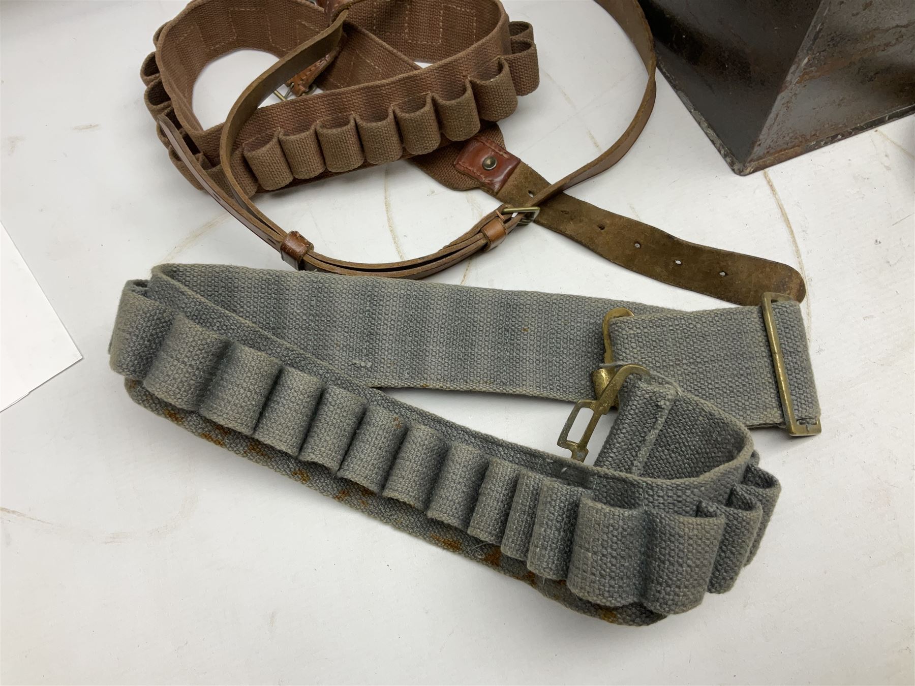 Assorted militaria including ten leather or canvas cartridge and other belts, maroon beret with 17th Lancers cap badge, modern bullet mould, leather and brass shot flask, two knives, shell cases, boomerang etc; in tin deed box