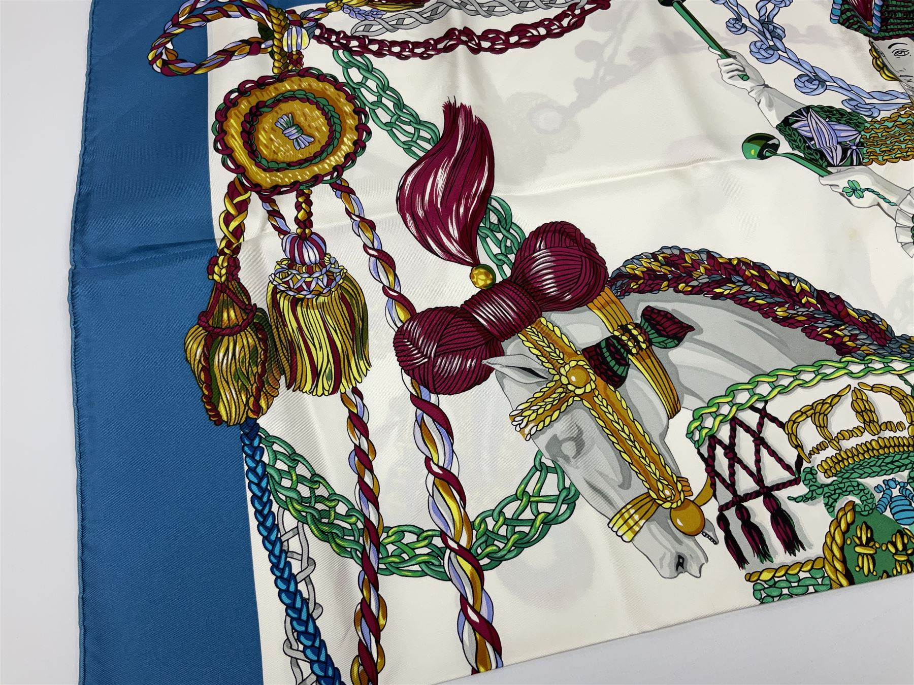 Hermès 'Le Timbalier' silk scarf, designed by Francoise Heron in 1961, printed with a central image of a gentleman on horseback donning extravagant dress, on white ground surrounded with colourful stylised knotted ropes, contained within peacock blue border, with rolled hand stitched edges and Hermes material label, 87cm square