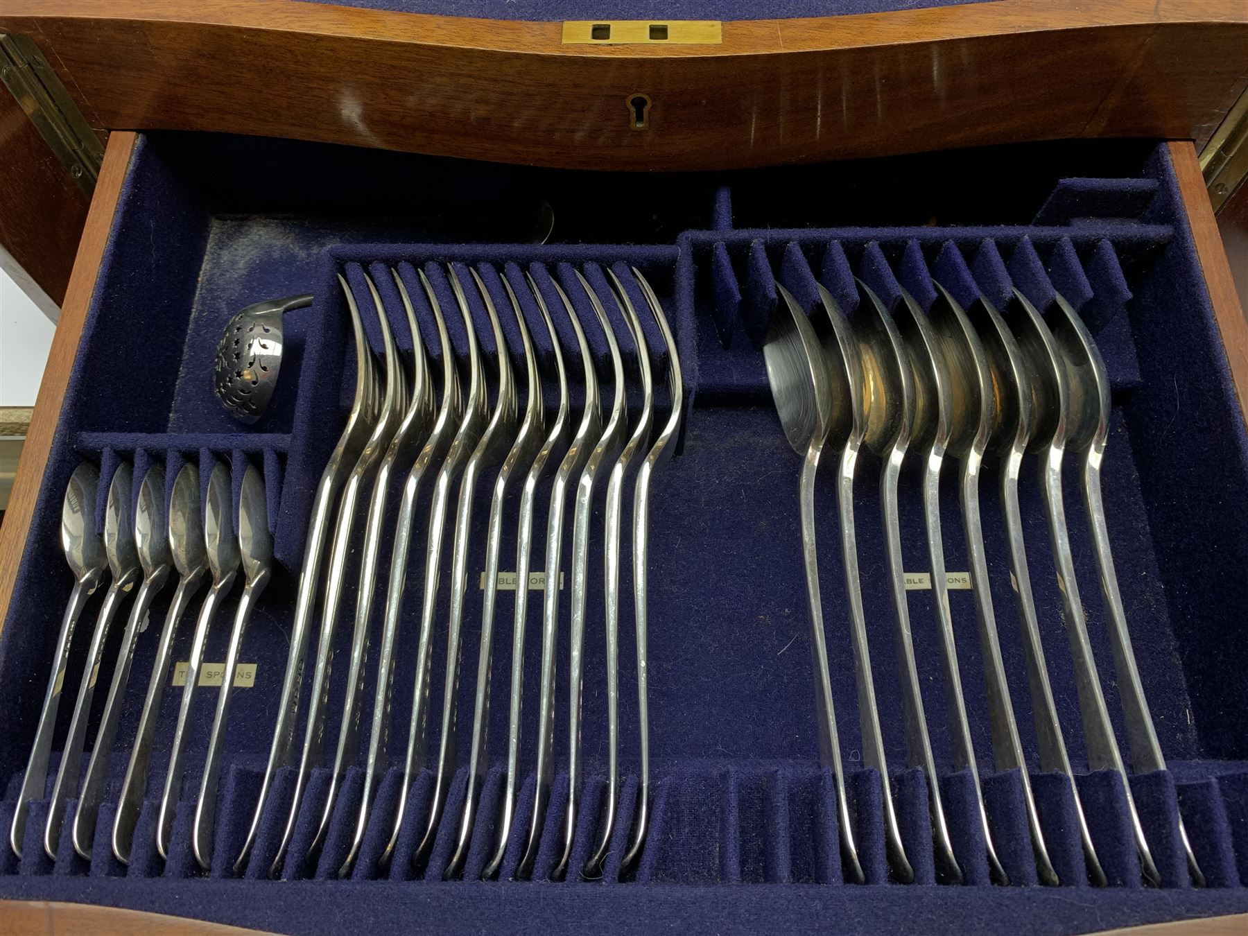Late 19th/early 20th century composite canteen of silver flatware, contained within an early 20th century mahogany serpentine fronted case with twin drop carry handles, and hinged cover with boxwood stringing and central inlaid shell motif, above a single drawer with twin ring handles and Wellington style locking system, the cover and drawer opening to reveal plaque for Spink & Sons Ltd London, and fitted interior containing ivory handled knives, ivory handled carving set, and silver Hanoverian and Old English pattern cutlery, each with engraved monogram to terminal, hallmarked London, makers Spink & Son (John Marshall Spink), Goldsmiths & Silversmiths Co, and Chawner & Co (George William Adams), various dates ranging 1880-1923, gross weighable silver 92.59 ozt (2880 grams)