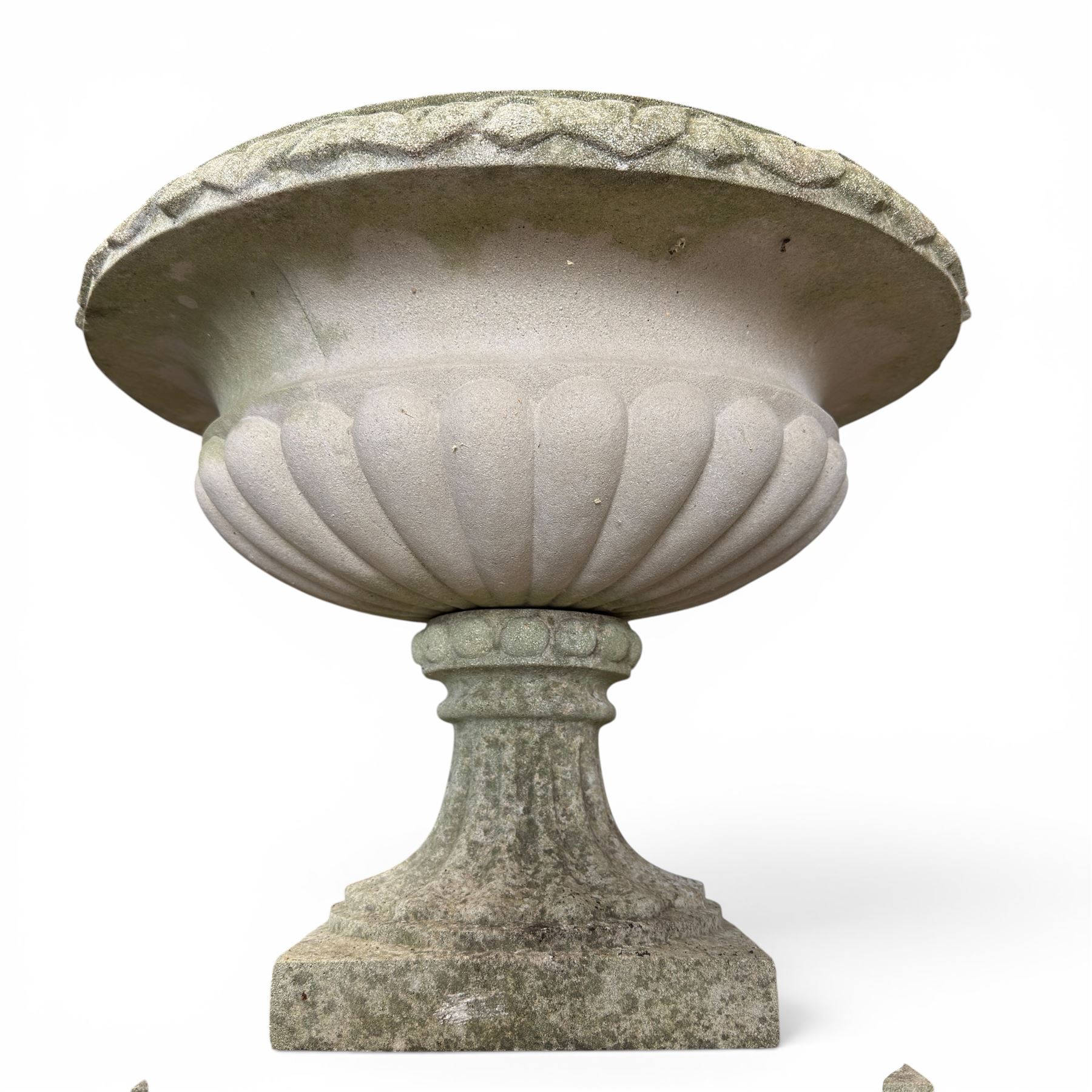 Pair of weathered cast stone Neoclassical design garden Kylix shape urns, foliate moulded rim over a gadrooned underbelly, the scalloped socle over a rectangular pedestal with faux-panelled sides, stamped with stylised ‘H’ monogram