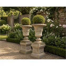 Pair of weathered composite stone campana urns on pedestals, the flared egg-and-dart rim o...