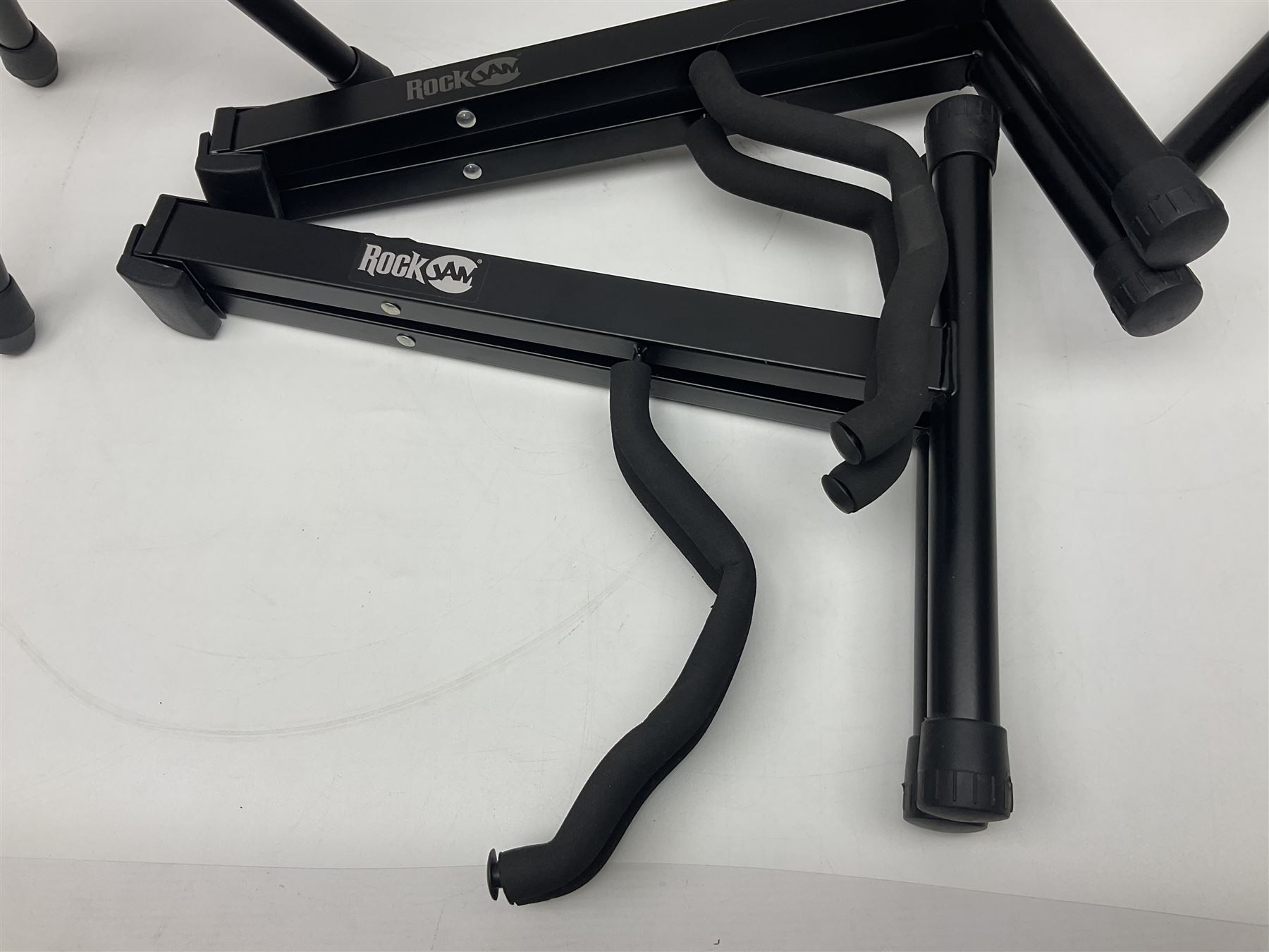 Four folding tubular guitar stands, two by RockJam; and folding tubular saxophone stand (5)