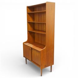 Mid 20th century Scandinavian teak bookcase cabinet in the manner of Johannes Sorth, the upper section with three open shelves over a shaped fall to a lower cupboard enclosed by sliding doors with recessed circular handles, raised on tapering supports