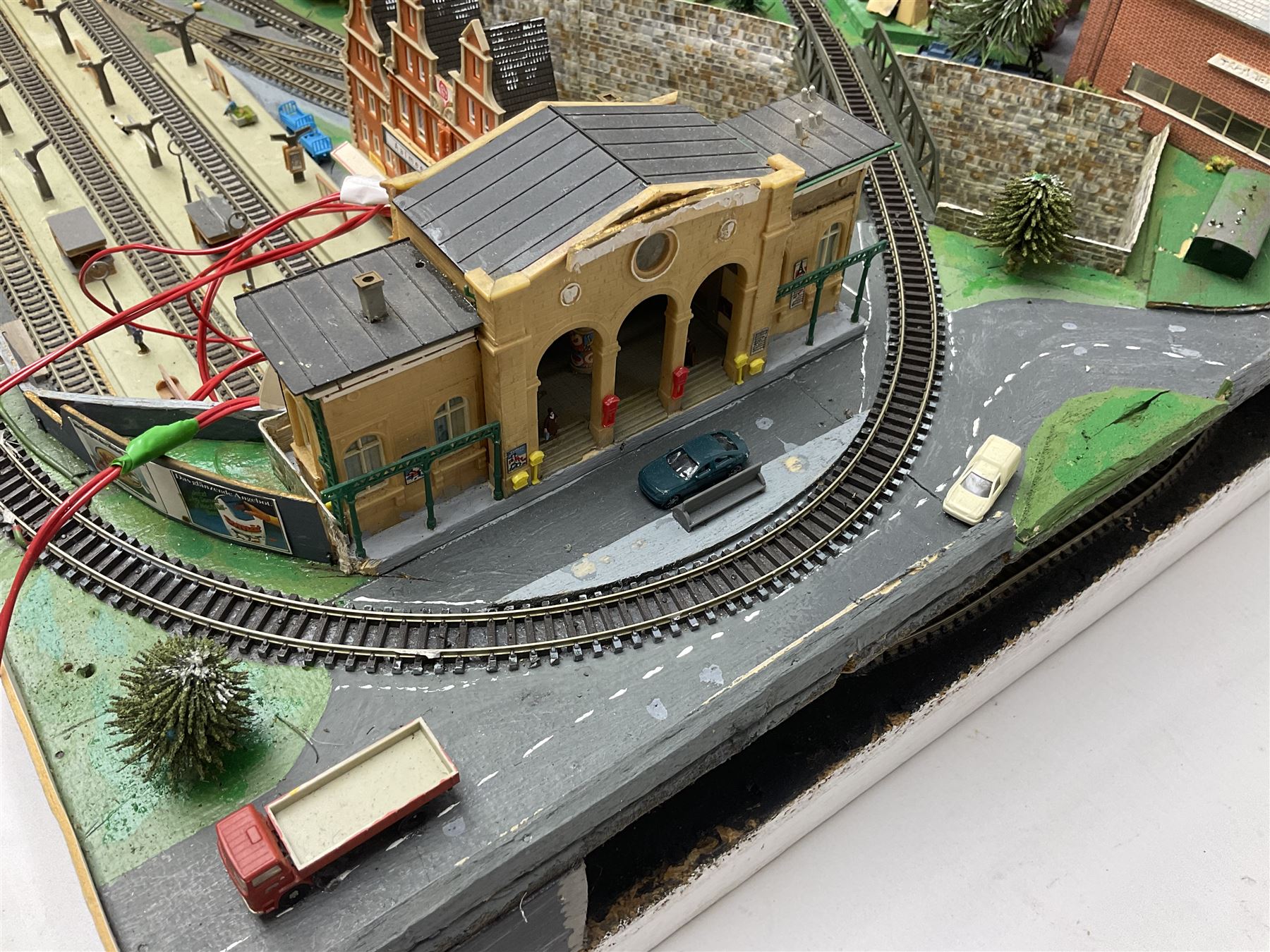 Table top 'N' gauge continental scenic layout as a split level town with various loops of track, station with numerous platforms, engine shed, assorted buildings, roads with motor vehicles and figures, tunnels, trees, river with bridge, tram depot etc 122 x 52cm