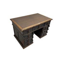 Late 19th century Gothic revival carved oak twin pedestal desk, rectangular top with inset writing surface and carved edges, central frieze drawer flanked by eight drawers, all with green man carved handles and extending trailing foliage, carvings of pineapple and lion mask corbels, the pedestals with panelled sides and back, on plinth bases