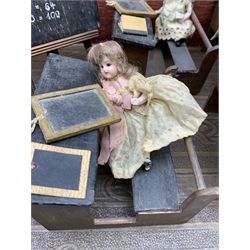 Late Victorian wooden school room setting with bisque head teacher and six German all bisque pupils each seated at a combined desk and chair with slate board, in a classroom furnished with chest of drawers, fire-surround, lectern, wall map, pictures, miniature books, school bell, chalk board on easel, wall clock etc, L70cm H28cm D28cm