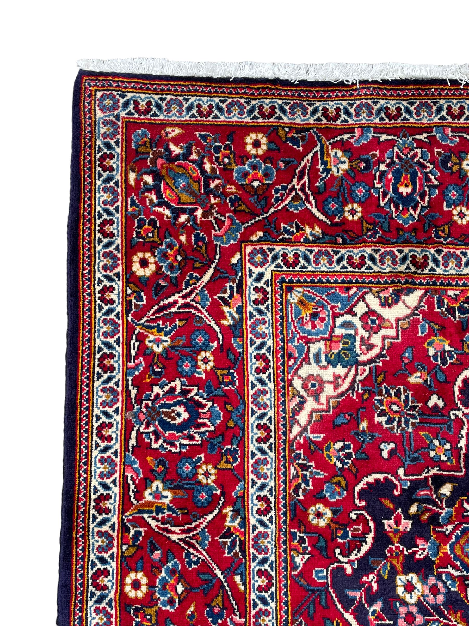 Persian indigo ground rug, the central crimson pole lozenge medallion surrounded by interlacing floral patterns, the main border with repeating plant motifs connected by scrolling branches