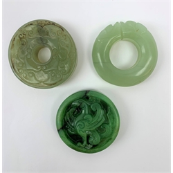 Two jadeite bi discs, largest D5.5cm, together with a nephrite jade disc with carved zoomorphic detail, D5cm. (3). 

