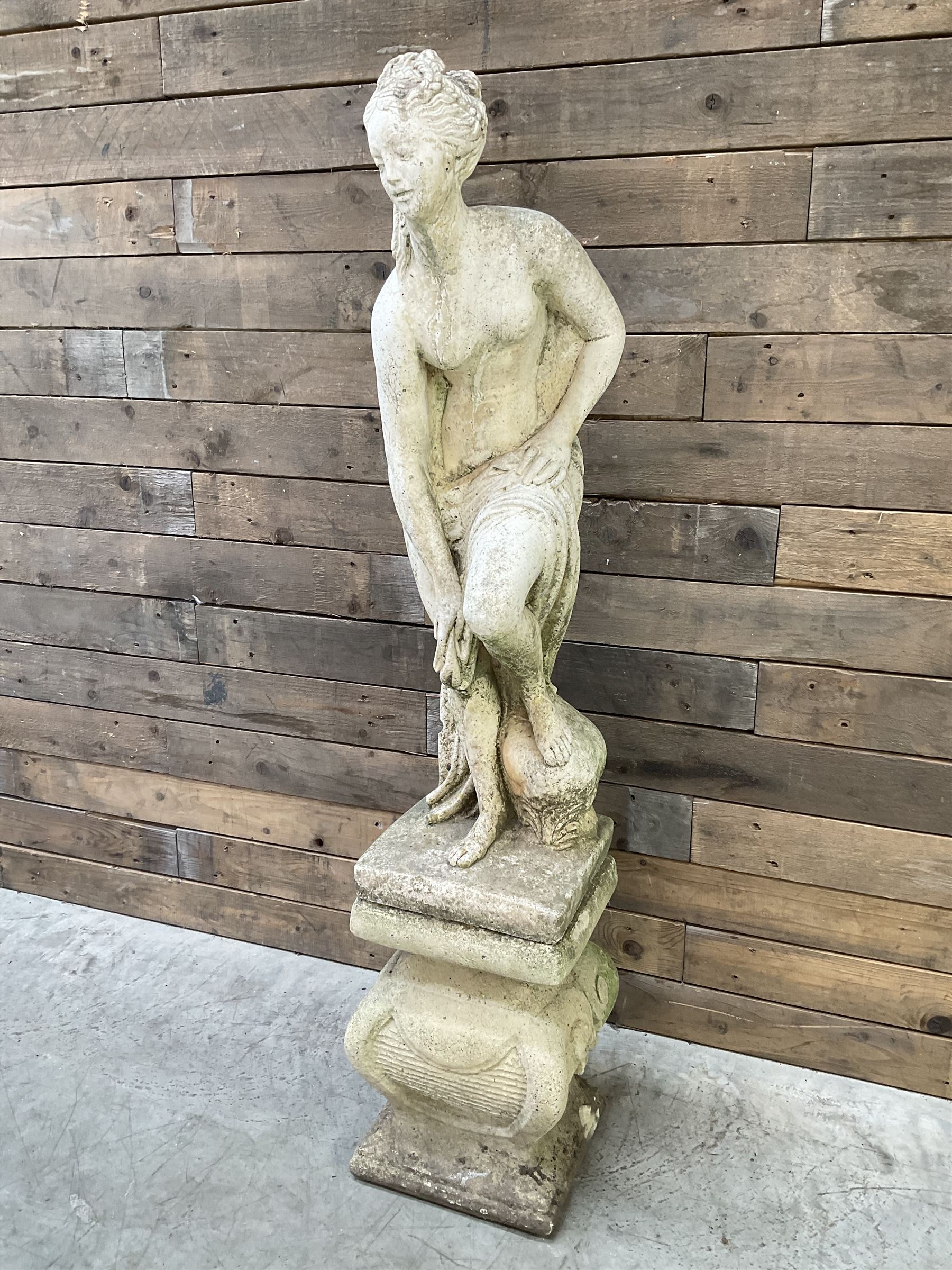 Cast stone garden statue of partially draped classical female figure on ornate pedestal 