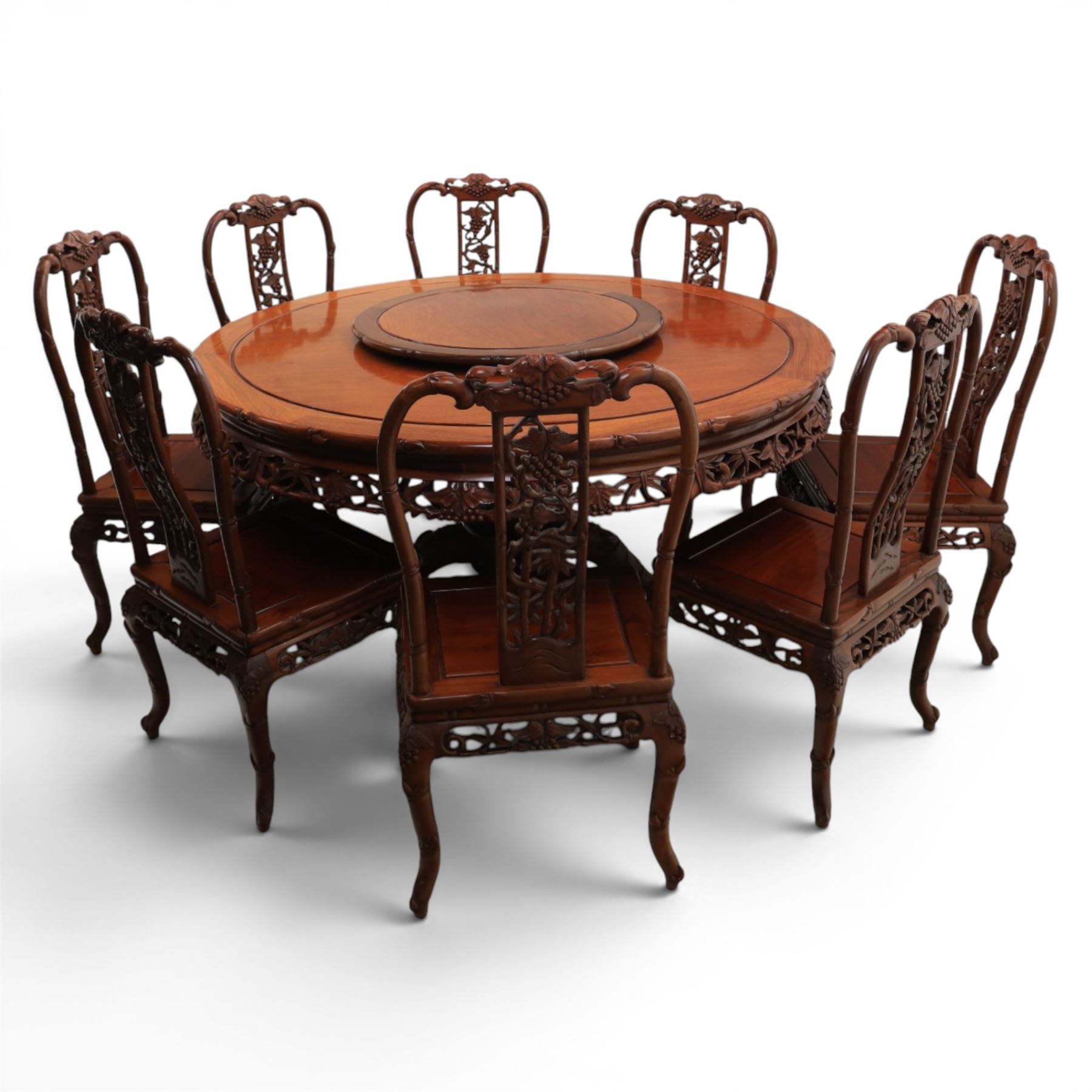 20th century Chinese ornately hardwood dining table and chairs, circular table with 'Lazy Susan' top with pierced carved frieze, raised on a quadriform base with carved foliate detail, the chairs en suite with carved pierced detailing  