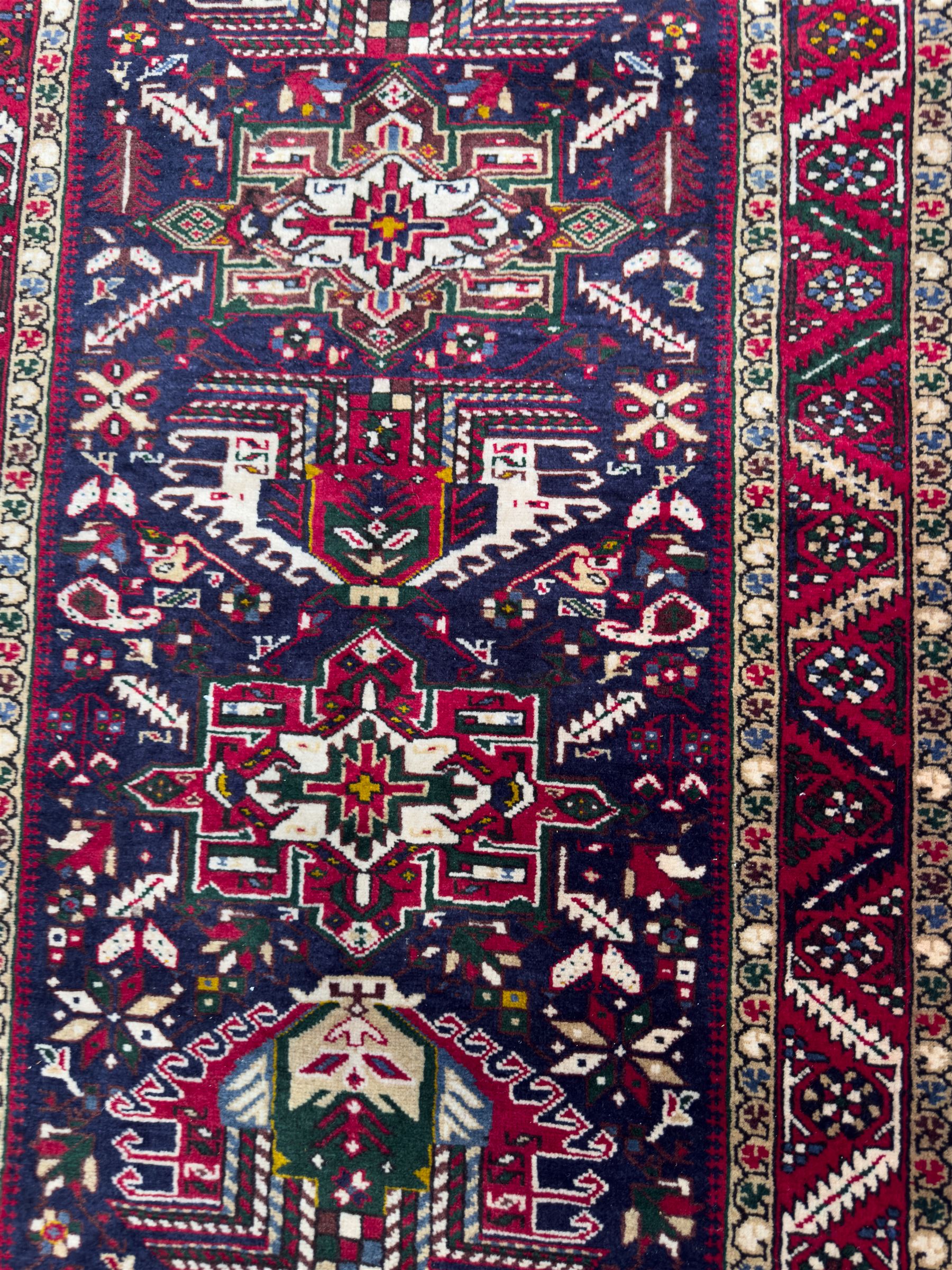 Northwestern Persian Heriz hand-knotted runner, dark indigo field with a series of linked stepped medallions in madder red, ivory, and green, flanked by angular floral motifs, within a madder red border of stylized rosettes and geometric vine motifs 405cm x 95cm