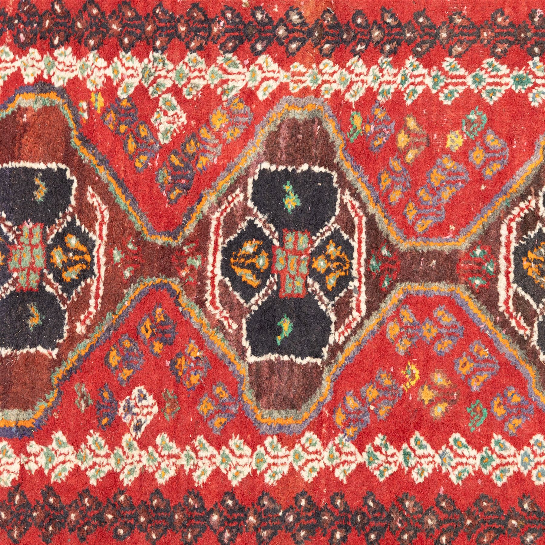 Northwestern Persian village rug, madder red field, with serrated central panel enclosing three linked lozenge medallions, polychromed spandrels, ivory border, and geometric guard stripes  
