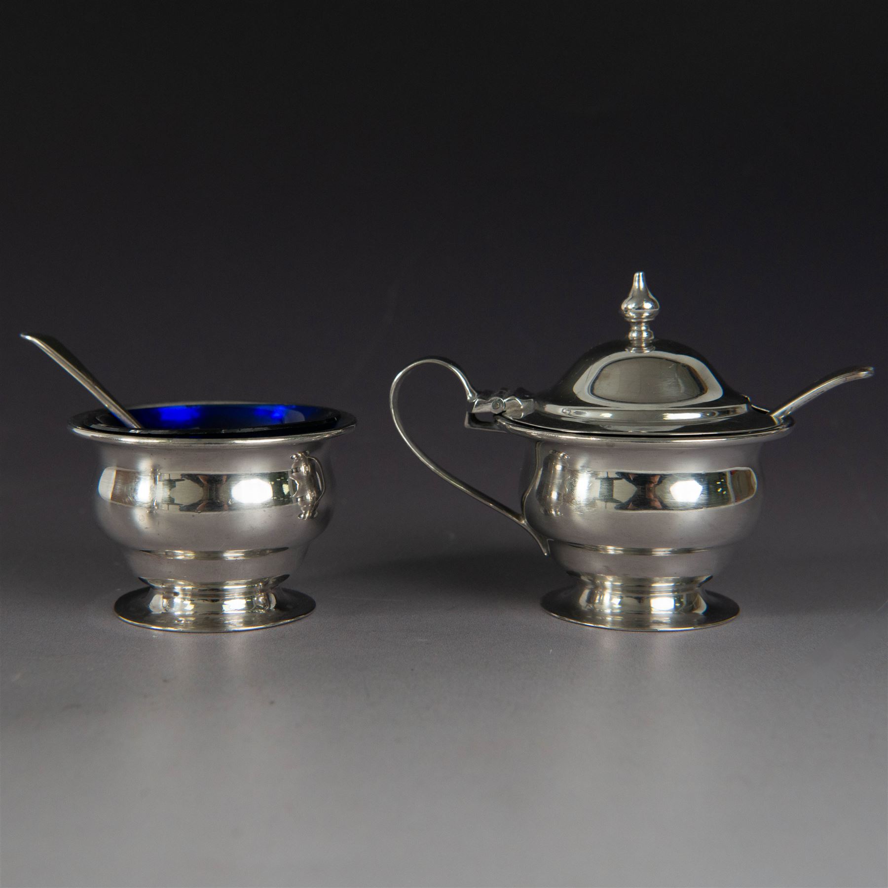 1930s silver three piece cruet set, comprising pepper shaker, open salt and mustard pot and cover, all of circular form upon circular spreading feet, hallmarked 	Atkin Brothers, Sheffield 1930, with two silver condiment spoons and blue glass liners