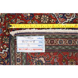 North West Persian Tabriz hand-knotted rug, ivory field with a central lozenge shaped medallion in indigo and madder red, issuing an ornamented arrangement of Herati style motifs, rosettes and angular floral elements, conforming spandrels on an ivory ground, main border in madder red with stylized vinery and palmettes, flanked by multiple guard border, with cotton fringe ends 