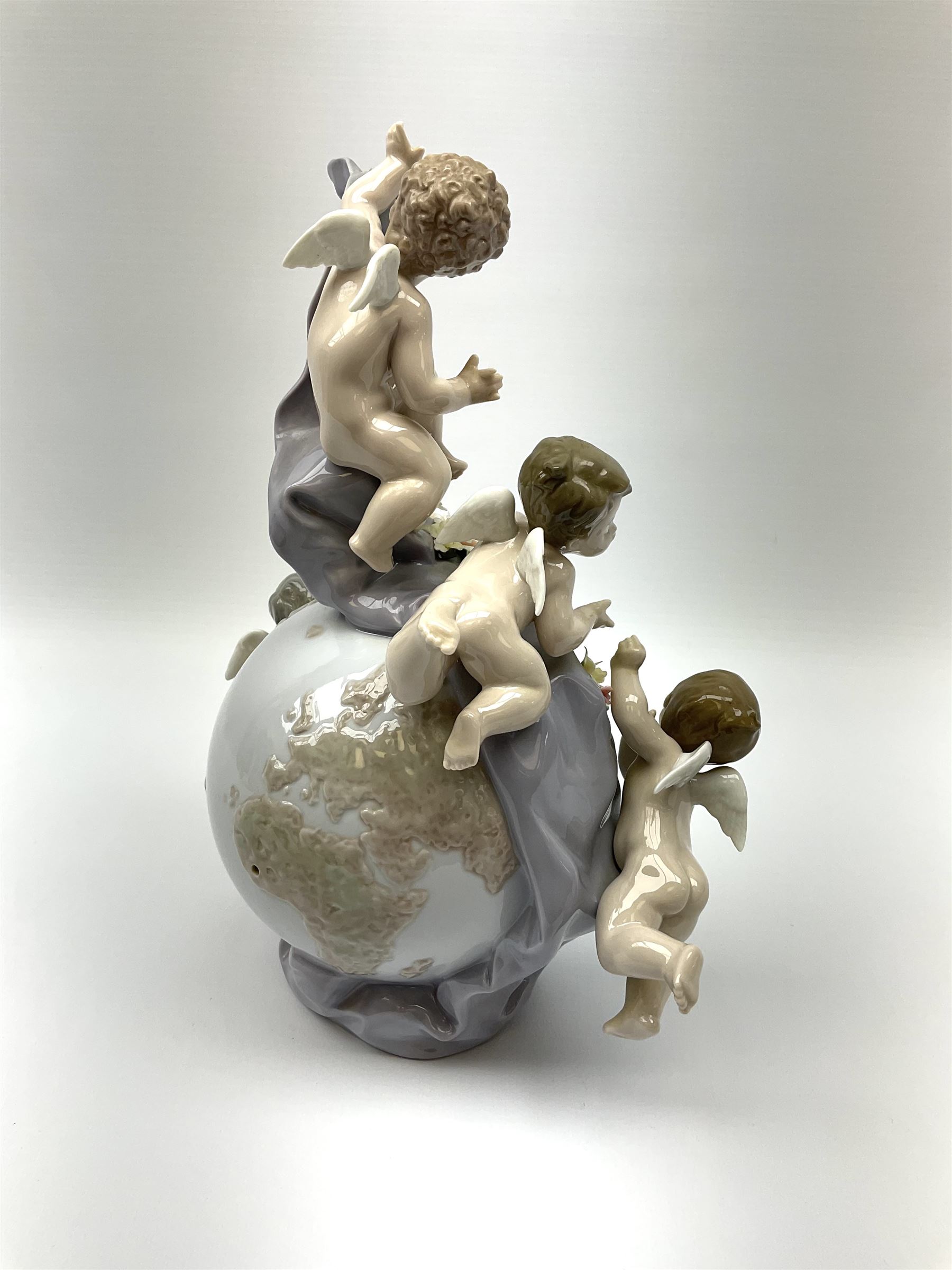 A Lladro mantel clock modelled as a globe with inset clock, surmounted by four putti and floral garlands, with blue printed mark and impressed 5973 beneath, H29cm.