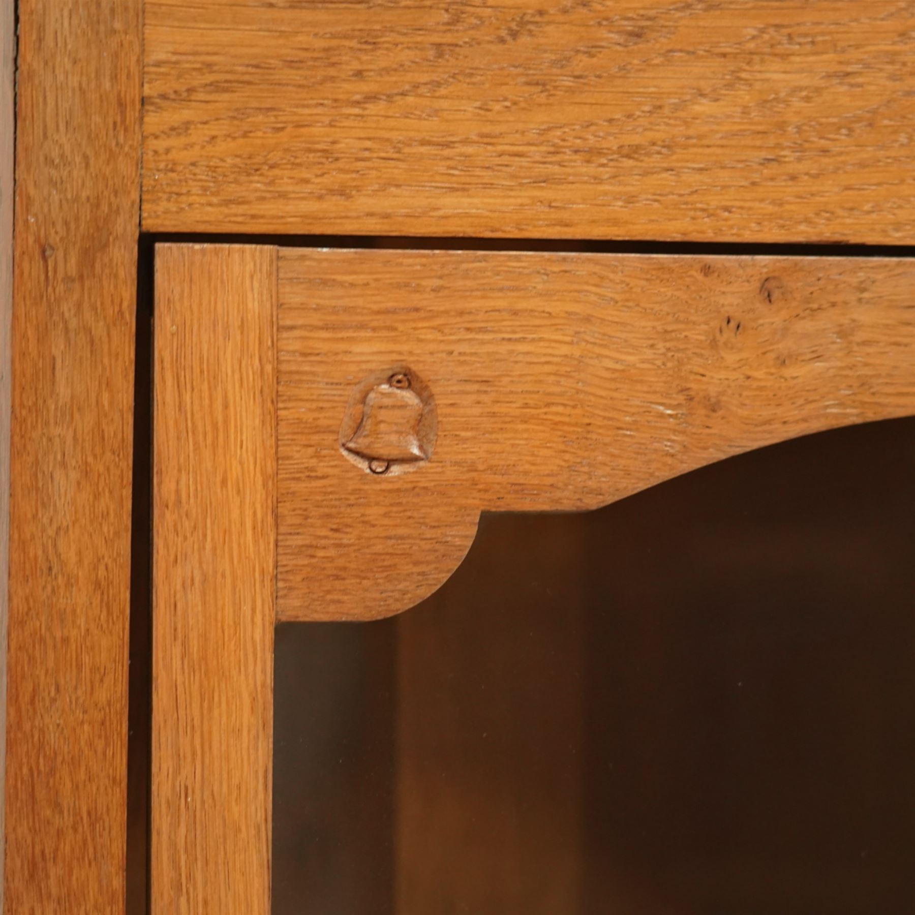 Yorkshire oak corner cabinet, chamfered triangular top above a single glazed door with shaped arched upper rail, enclosing two shaped fixed shelves, plain sides and back, raised on a moulded plinth base, carved with a bell signature