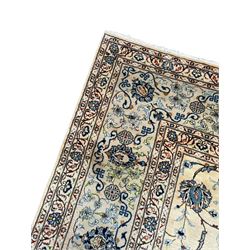 Persian Kashan ivory ground carpet, the field decorated with swirling foliate patterns and stylised plant motifs, scrolling border decorated with palmettes, within floral pattern guard stripes 