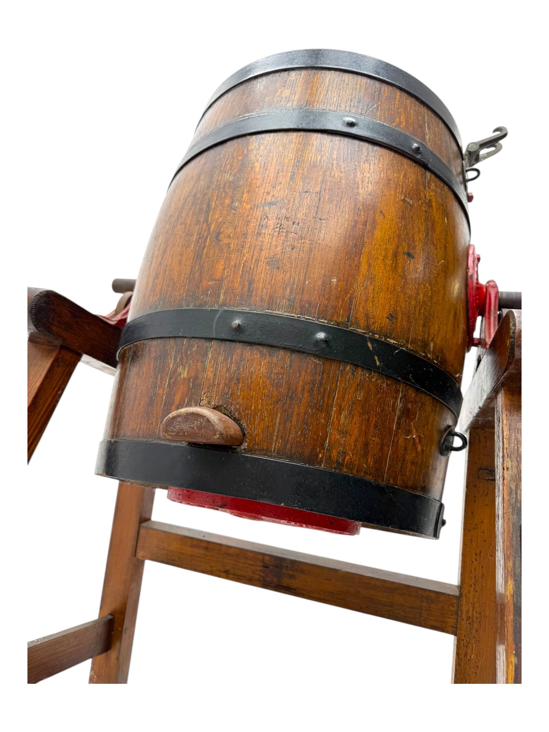 19th century oak and cast iron rotary butter churn, with coopered barrel body, domed lid with filler opening and cast iron securing arms, on tilting iron-mounted frame with crank handle and support rails