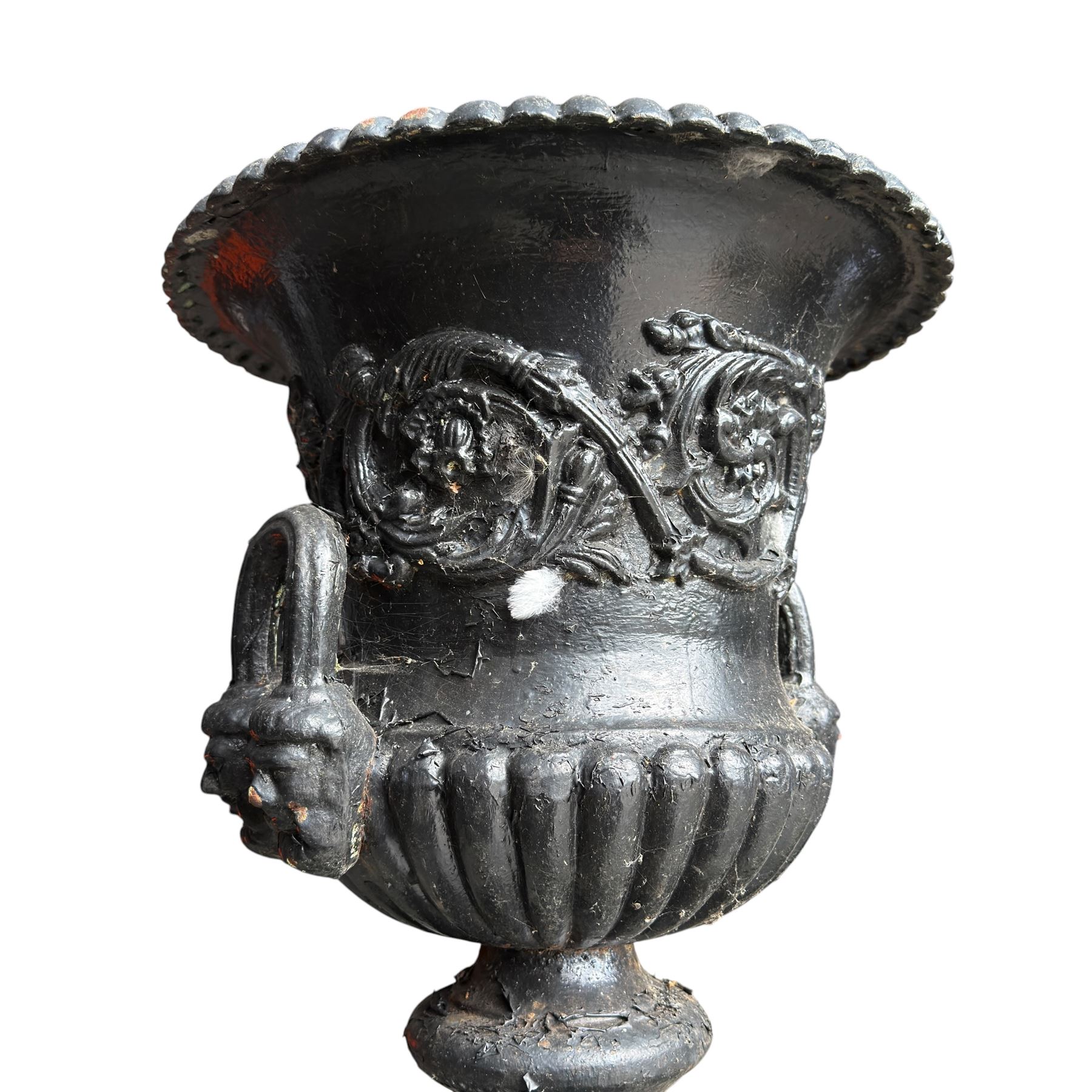 Pair of Victorian cast iron campana form garden urns, the gadrooned flared edge over a scrolling acanthus relief body, with twin male mask handles to each side, over a lobed underbelly with fluted socle, the rectangular pedestals with relief floral garlands and stepped base, in rustic black-painted finish, planted