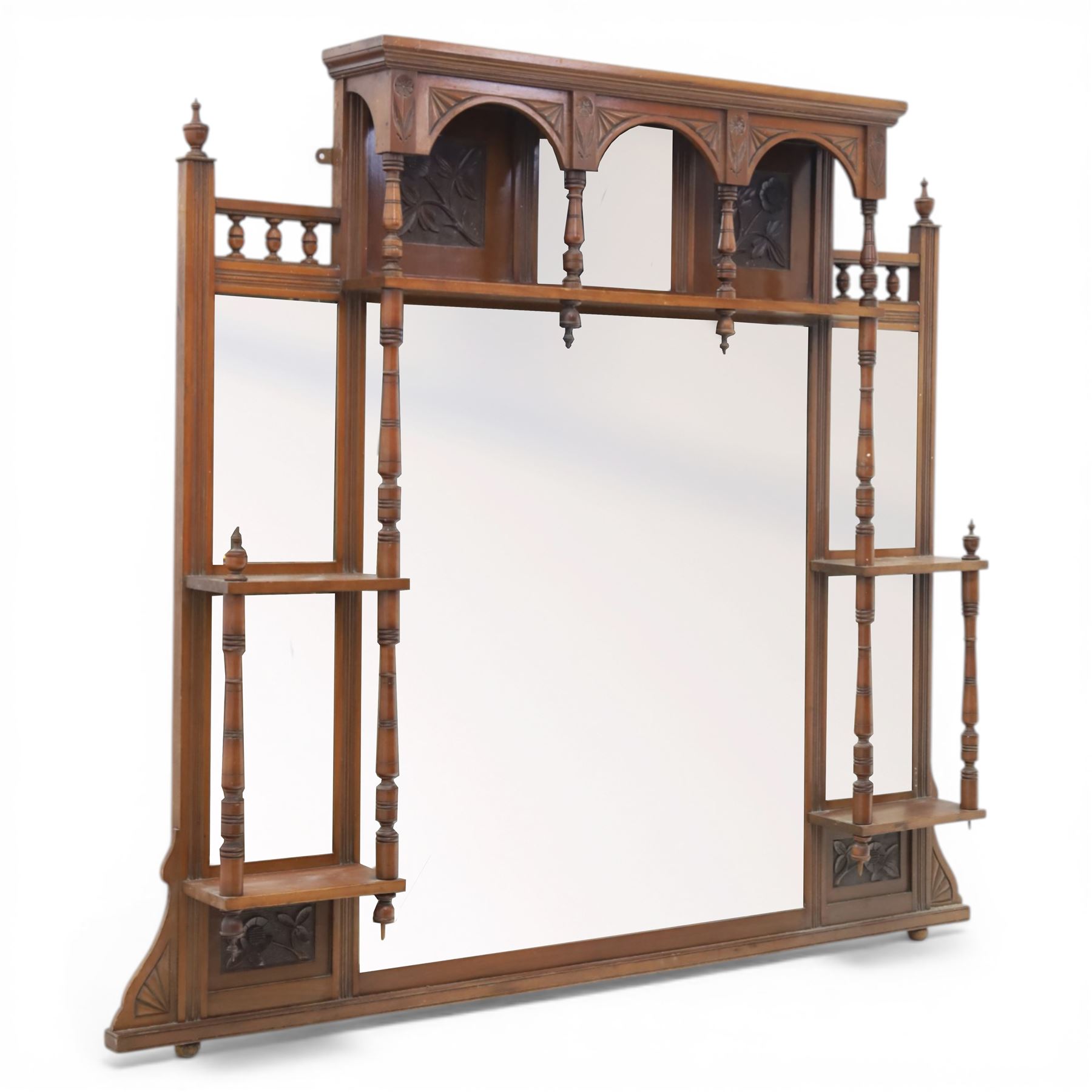 Edwardian walnut overmantel mirror, moulded cornice over three arched apertures with turned supports, flanked by open shelves with turned uprights and finials, carved foliate panels to the base