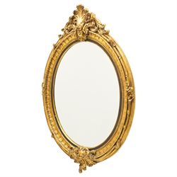 Pair of Rococo Revival gilt framed oval wall mirrors, the exuberant pediment formed of scrolling acanthus leaves and rocaille ornament, the oval bevelled plate set within with ebonised slip with outer repeating lappet decoration, over a rocaille cartouche terminal