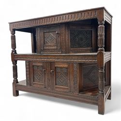 Early 20th-century  oak Jacobean two-tier revival court cupboard, rectangular top with carved notch and stylized foliate carved edge above a carved lozenge pattern frieze and a central cupboard with carved geometric designs and geometric carved panelled sides, above a carved panelled cupboard with two doors of similar geometric design, the whole flanked by two sets of stop-fluted baluster turned columns and supported on stile feet