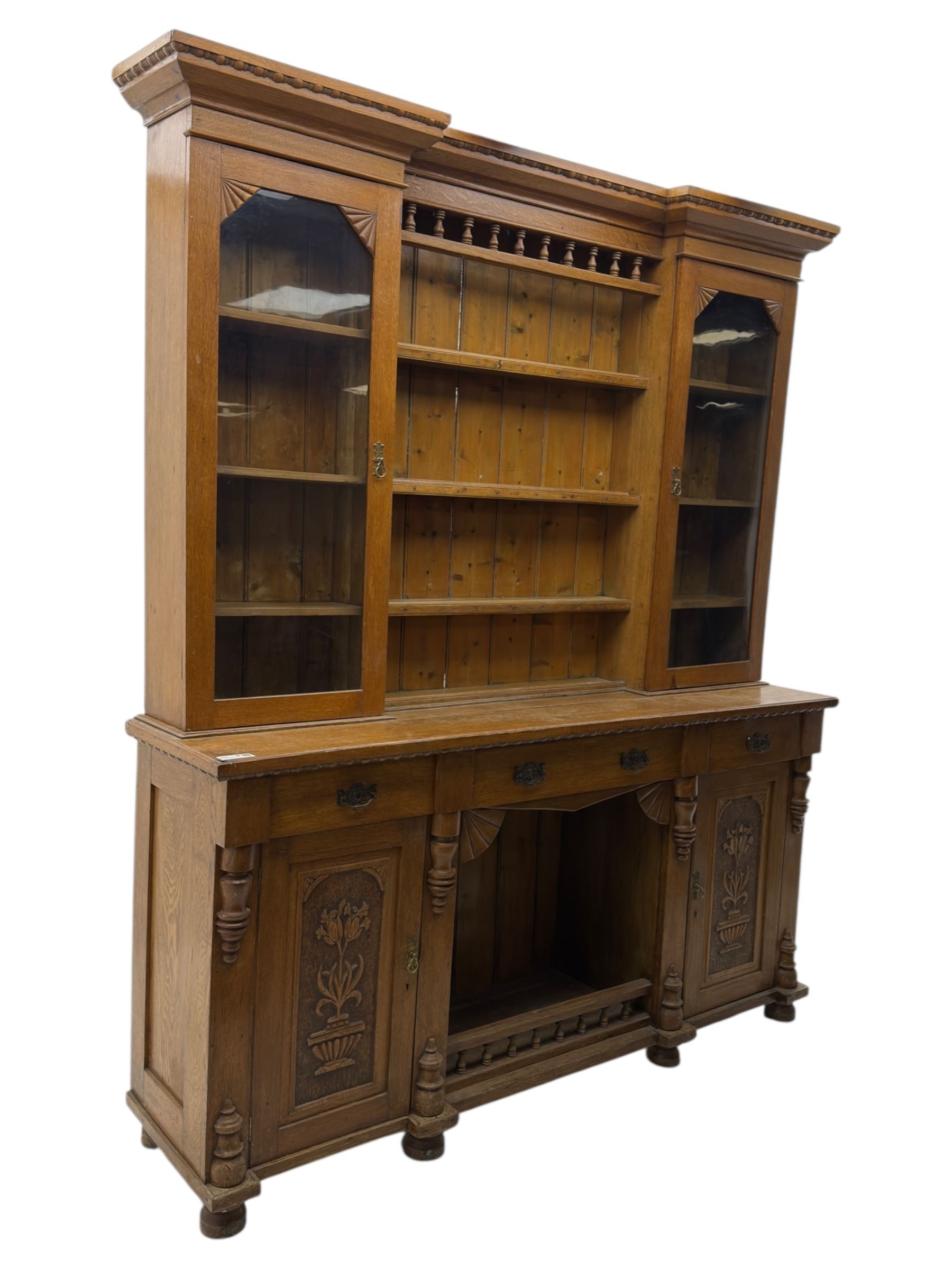 Late 19th century pine dresser, the projecting cornice with dentil and spindle moulded frieze above a three-tier plate shelves, flanked by glazed doors, the base fitted with three frieze drawers over arched apron and carved floral panelled cupboard doors, raised on turned feet