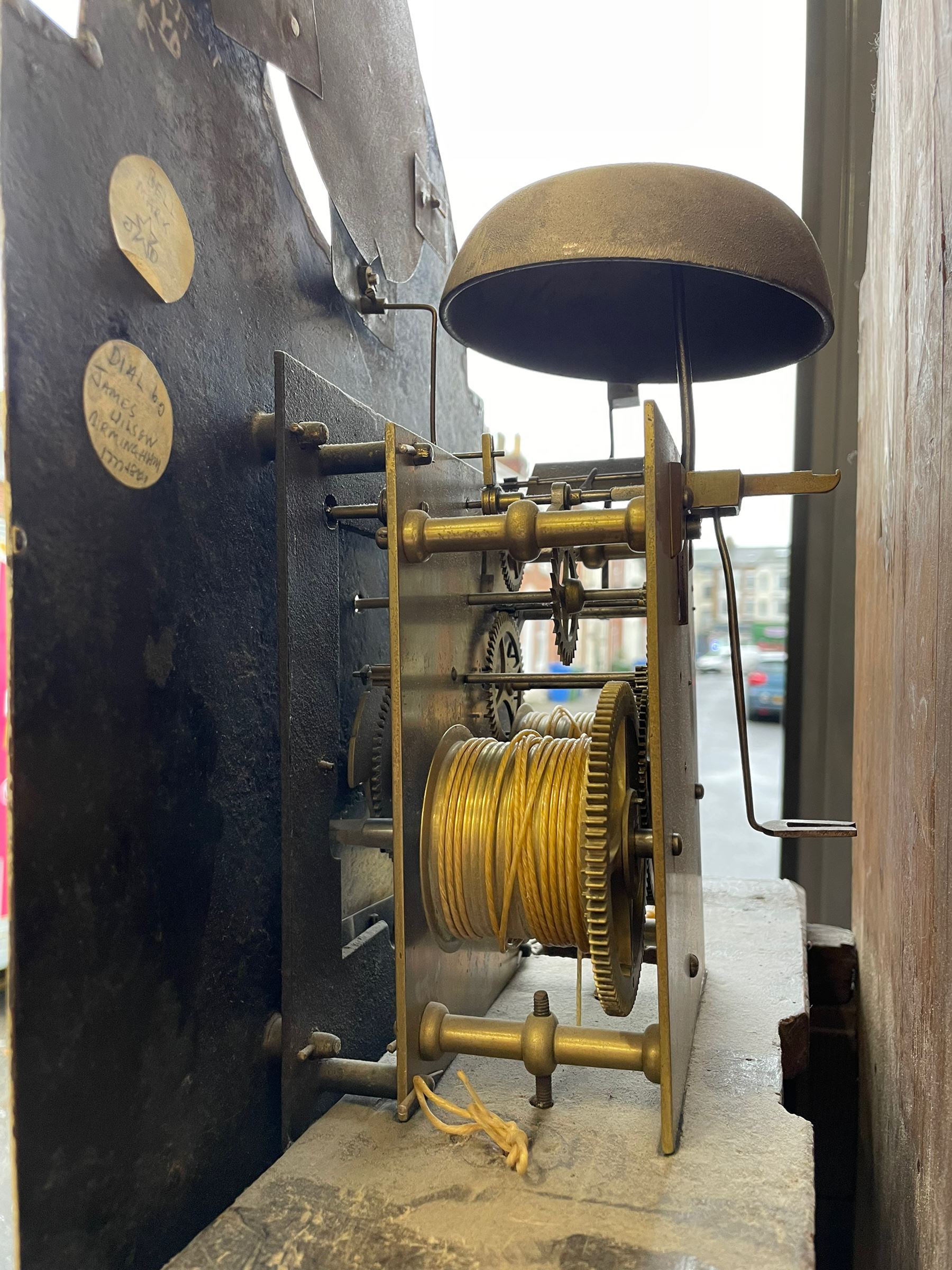 William Gostling of Diss  (Norfolk)-  Late 18th century 8-day oak longcase clock c1780-90, break arch top with scalloped cresting and three brass finials, glazed break arch hood door flanked by turned pilasters with brass capitals, trunk with a long trunk door and rounded top on a square plinth with an applied and shaped skirting, early painted Wilson of Birmingham dial with Roman numerals and five minute Arabic's, matching steel hands and second pointer, arched square ended calendar aperture with date disc behind, floral spandrels within gesso borders and a painted rocking automaton representing Mercury to the break arch, dial pinned via a false plate to a weight driven rack striking movement with a recoil anchor escapement, striking the hours on a cast bell. With pendulum weights and key. 
William Gostling (II) is recorded as working in Diss from 1774 to 1797, succeeded by widow Anne and son George . The dial of this clock is illustrated and discussed in detail in M.F. Tennants book 