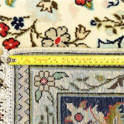 Central Persian Kashan hand-knotted carpet, ivory ground, with an all-over floral field centred by a subtle shaped medallion, surrounded by scrolling foliate and floral motifs incorporating rosettes, palmettes and delicate vine work, enclosed by a dark navy border with repeating palmettes and meandering vines, flanked by floral guard stripes, with cotton fringes