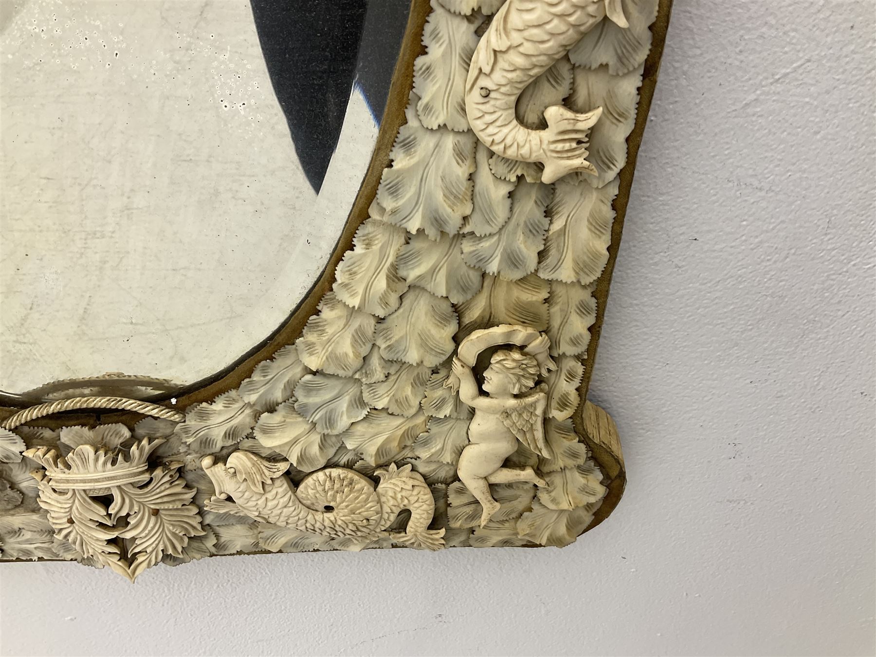 Pair 19th century French Dieppe bone and ivory wall mirrors, the oval bevelled mirror plates within rectangular frames with shaped tops, profusely decorated with ivory leaves, further detailed with carved bone armorial type crest inscribed 'SGOTORVM', putti, fish and mask heads, H81cm W48cm