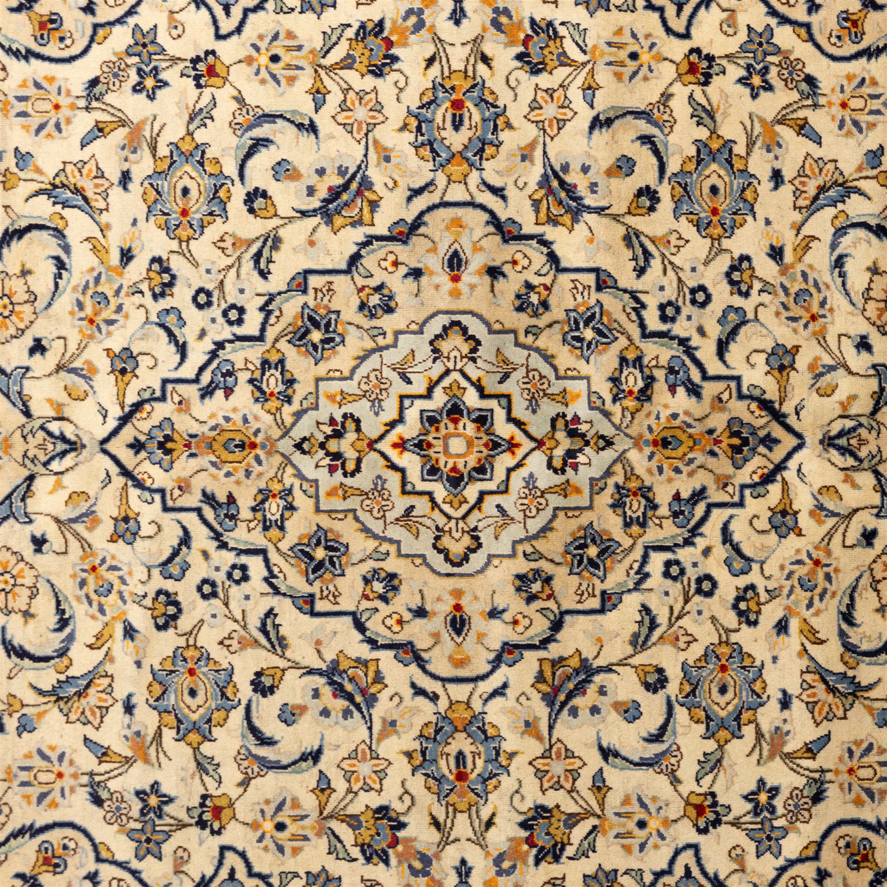 Central Persian Kashan hand-knotted carpet, ivory ground with central stepped floral medallion surrounded by scrolling vine work, palmettes, and stylized blossoms, field enclosed by a multi-border arrangement, wide main border decorated with repeating floral cartouches and foliate motifs, flanked by narrow guard stripes, with cotton fringe ends