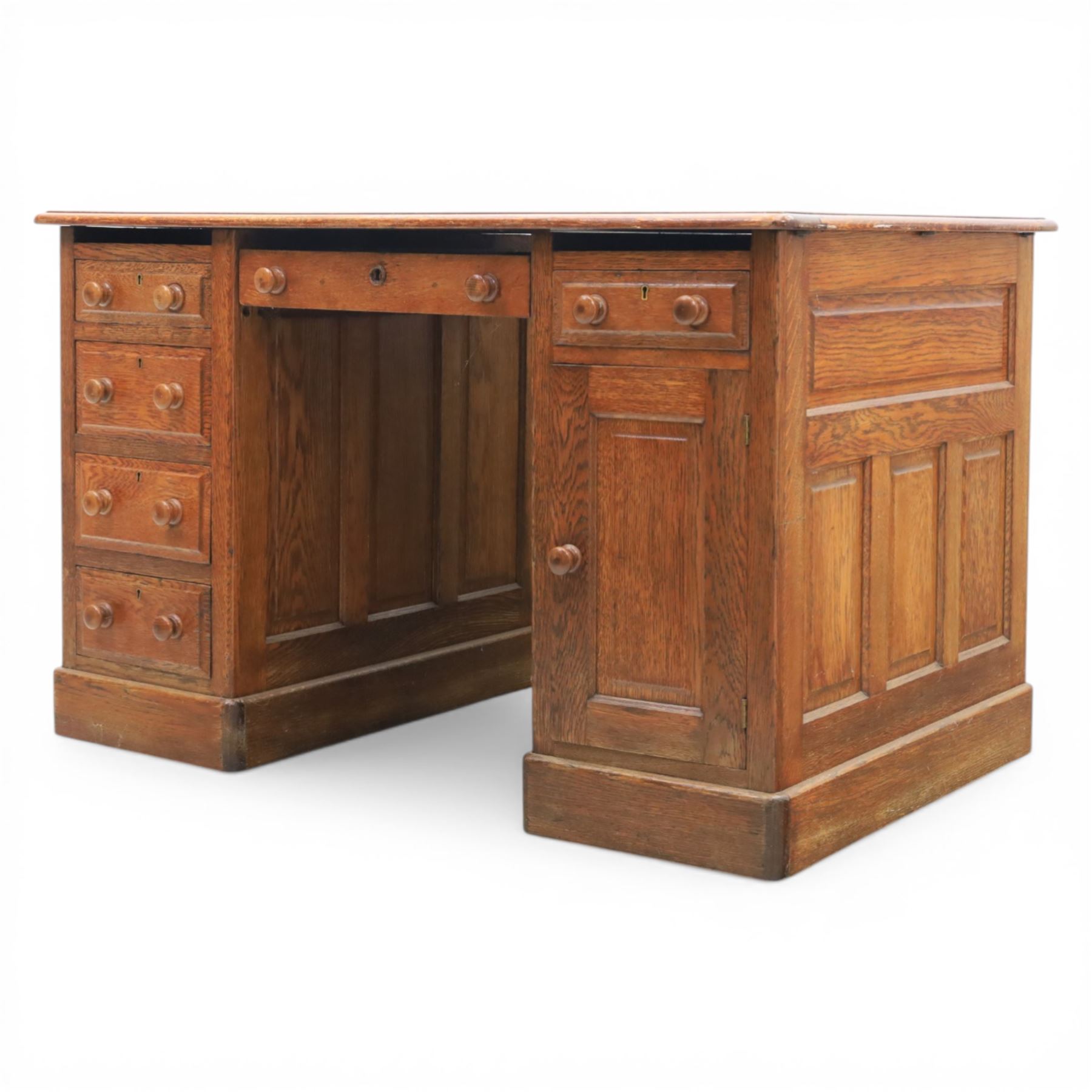 20th century oak compact pedestal desk, tooled green leather inset top, above a single frieze drawer, with a bank of four graduated drawers and a drawer and cupboard, panelled sides raised on castors