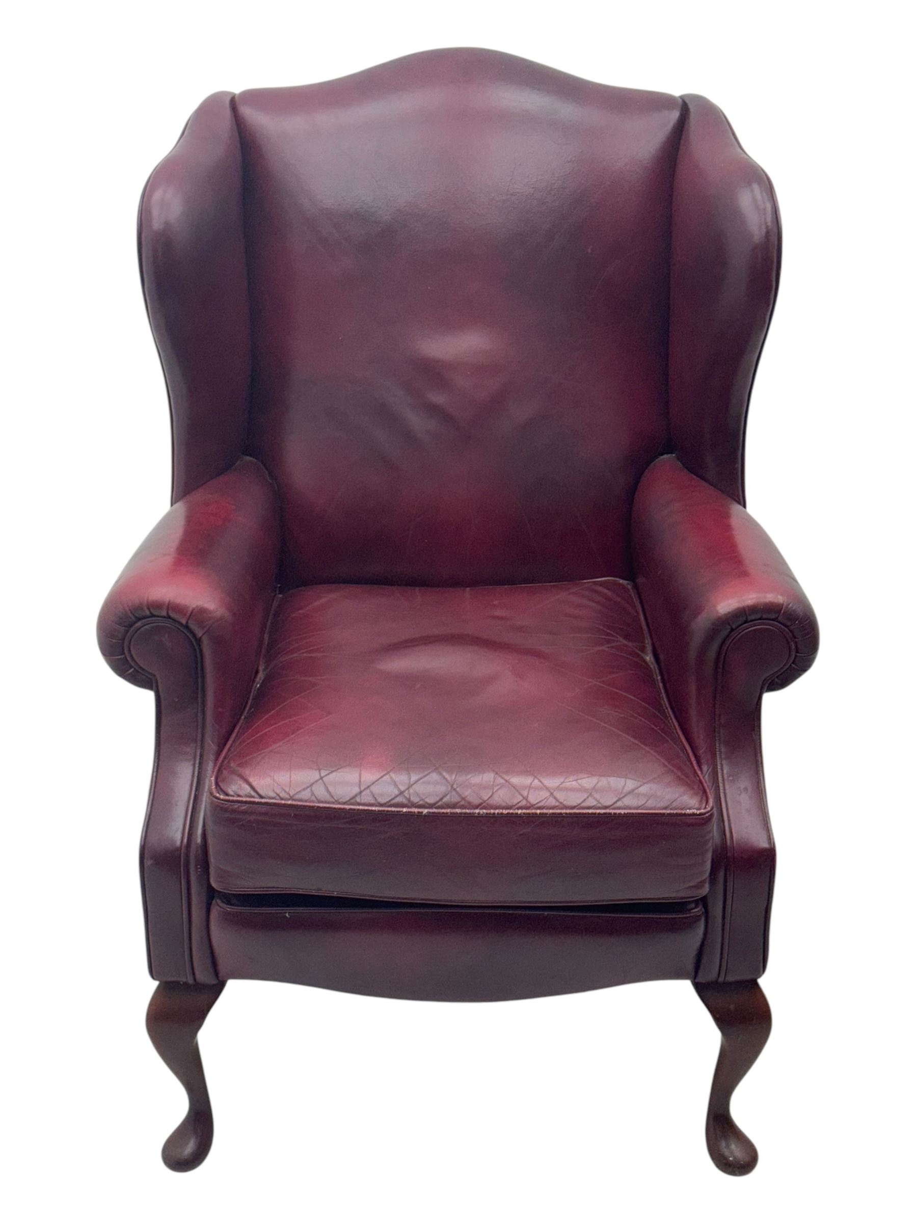 Mid-20th century leather wingback armchair, upholstered in deep burgundy leather, featuring a shaped backrest and scrolled armrests, raised on mahogany cabriole front supports