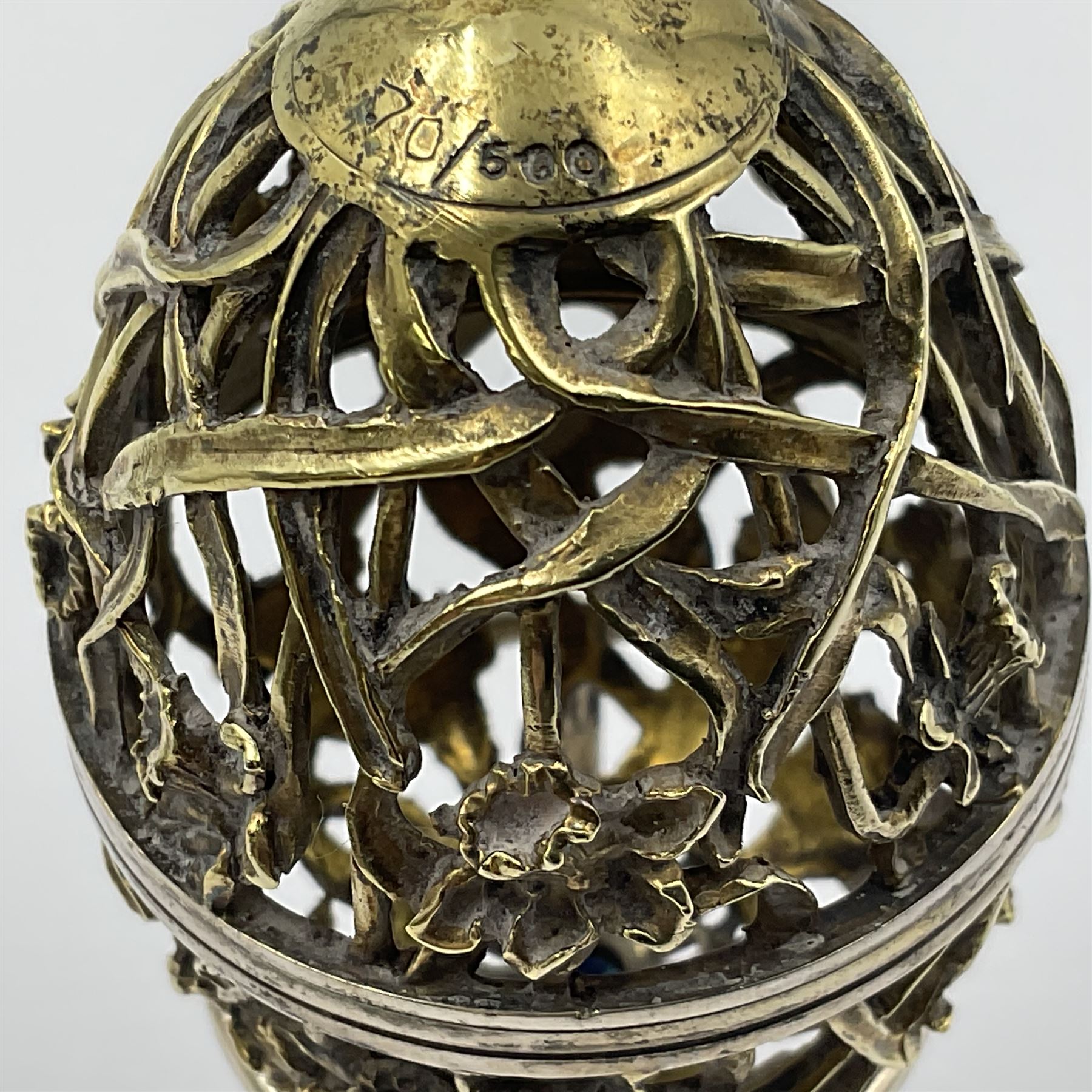 Modern silver limited edition Easter egg, no. 70/500, the gilt openwork body decorated with daffodils and detachable cover with pierced circular panel set with a single faceted blue stone, opening to reveal a gilt interior, upon silver stand with three scrolling pad feet, each hallmarked St James House Company, London 1980, height including stand 8cm