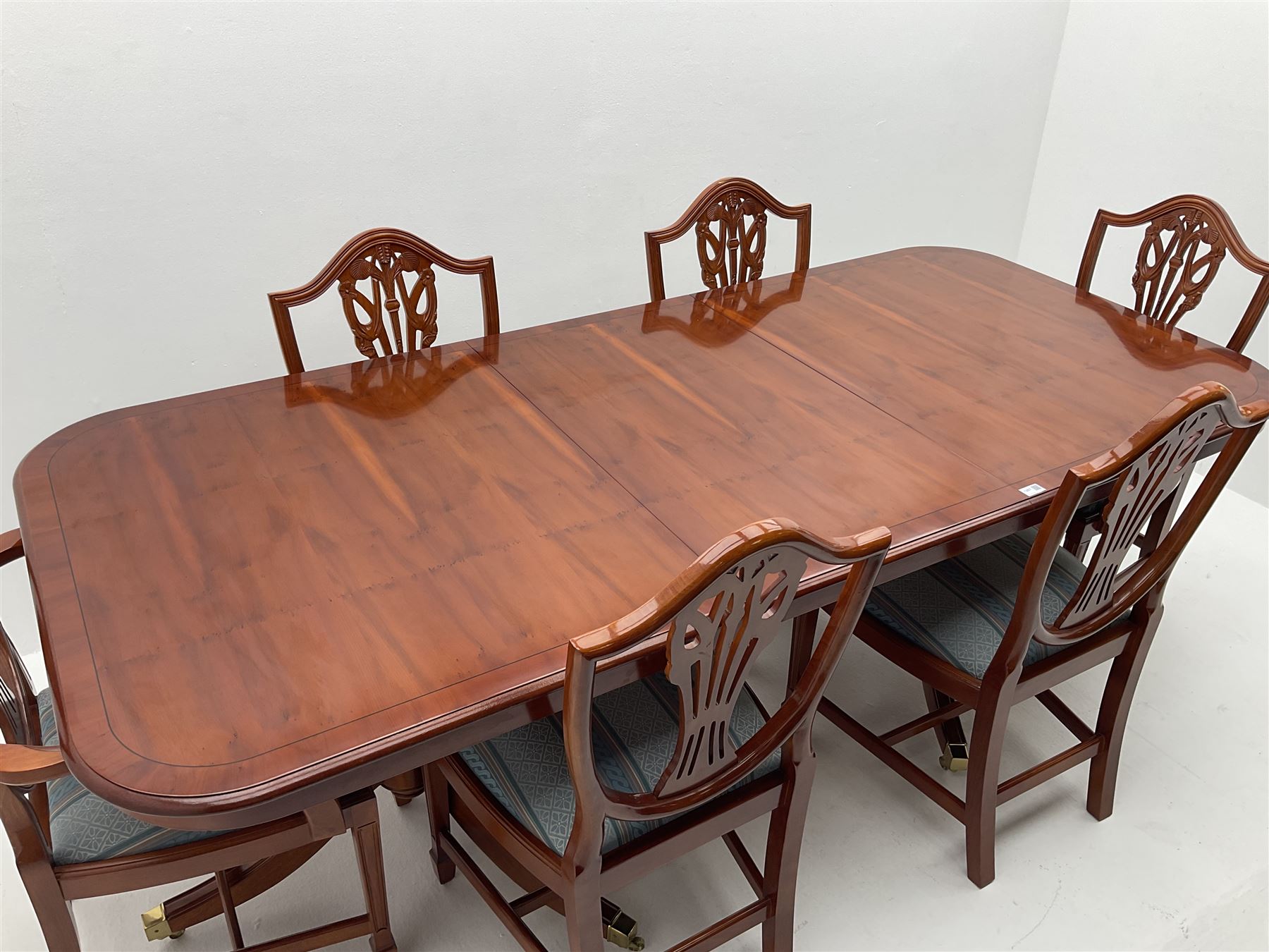 Yew wood twin pedestal extending dining table, shaped supports and brass castors (W216cm, D100cm, H77cm) and six (4+2) chairs, shaped back and upholstered in patterned fabric raised on fluted supports (W52cm)