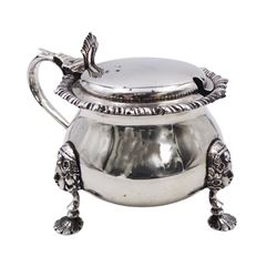 1920's silver mustard pot and cover, of bellied form with oblique gadrooned rim and capped scroll handle, the palmette thumbpiece lifting the slightly domed cover to reveal a blue glass liner, upon three mask mounted shell pad feet, hallmarked Mappin & Webb Ltd, London 1923, H7.5cm, approximate weight excluding liner 4.88 ozt (151.7 grams)