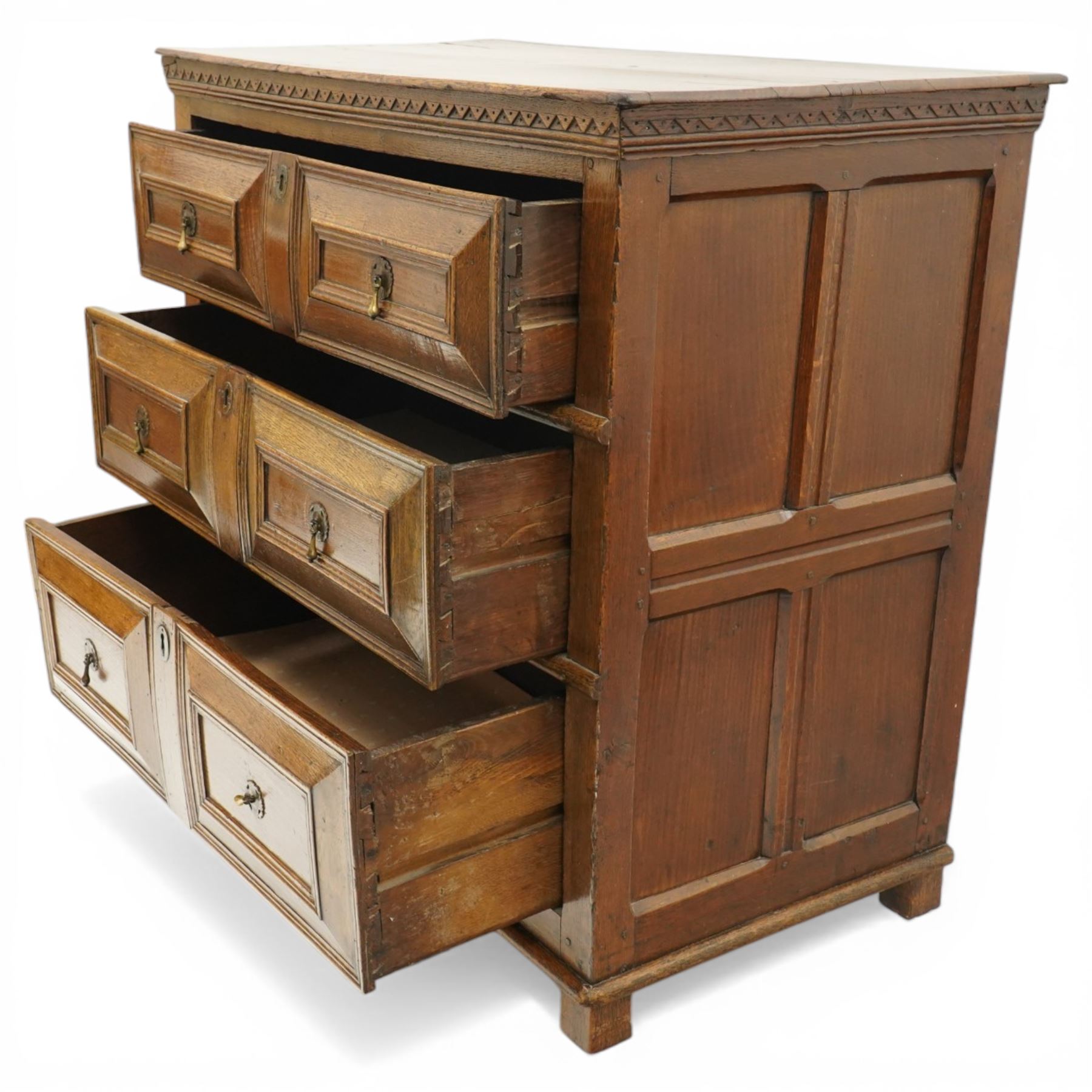 18th century oak chest of drawers, rectangular plank top with chip carved frieze, fitted with three long geometrically panelled drawers with applied mouldings, later brass drop handles, on stile supports, panelled sides and boarded back