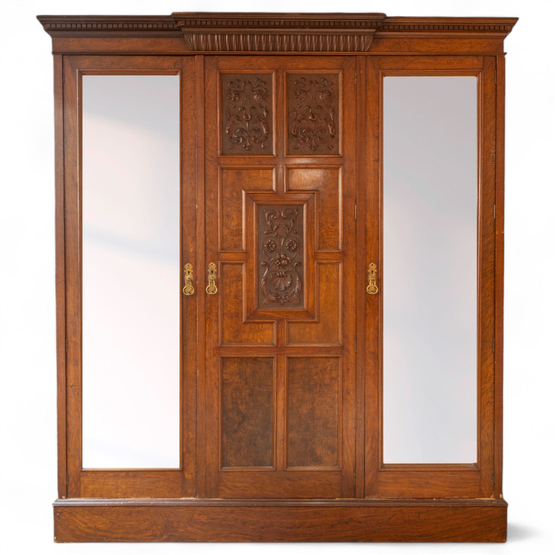 Late Victorian oak and burr oak three-section mirror wardrobe, central door with three carved panels with shell and acanthus decoration, fitted with four drawers and four tray drawers, linen sides with bevelled mirrored panel doors with hanging space, plinth base, and dental cornice