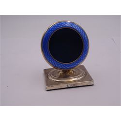 1920's silver pocket watch stand, of circular form with blue guilloche enamel detailed front, upon a spreading stem and rectangular base, hallmarked Birmingham 1923, makers mark indistinct, possibly E. H & Co, H7cm