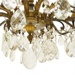 20th century Louis XV design gilt and patinated metal twelve-light chandelier, the foliate-cast baluster stem issuing scrolling acanthus branches with leaf-form drip pans, hung throughout with faceted glass pendants and lustre drops, suspended from chains beneath a foliate ceiling rose
