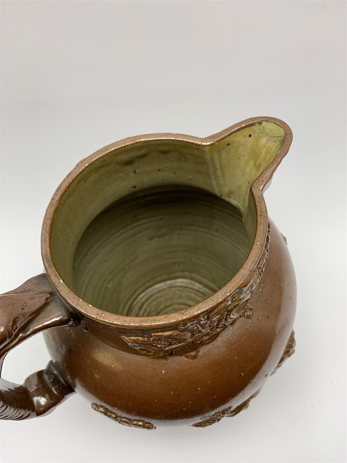 19th century salt glazed stoneware jug, with mask spout and greyhound modelled handle, the body decorated in relief with Royal Coat of Arms flanked by lions, the rim with the flowers of the union, roses, thistles and shamrocks, H26.5cm