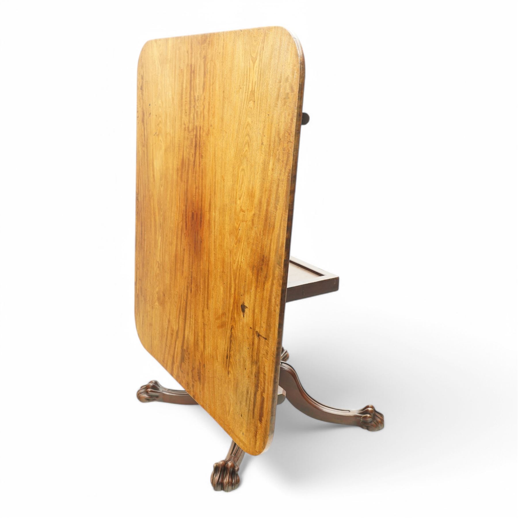 Large Regency mahogany breakfast table, figured rectangular tilt-top with rounded corners, on wide turned pedestal with four out-splayed moulded supports, paw carved terminals with recessed castors 